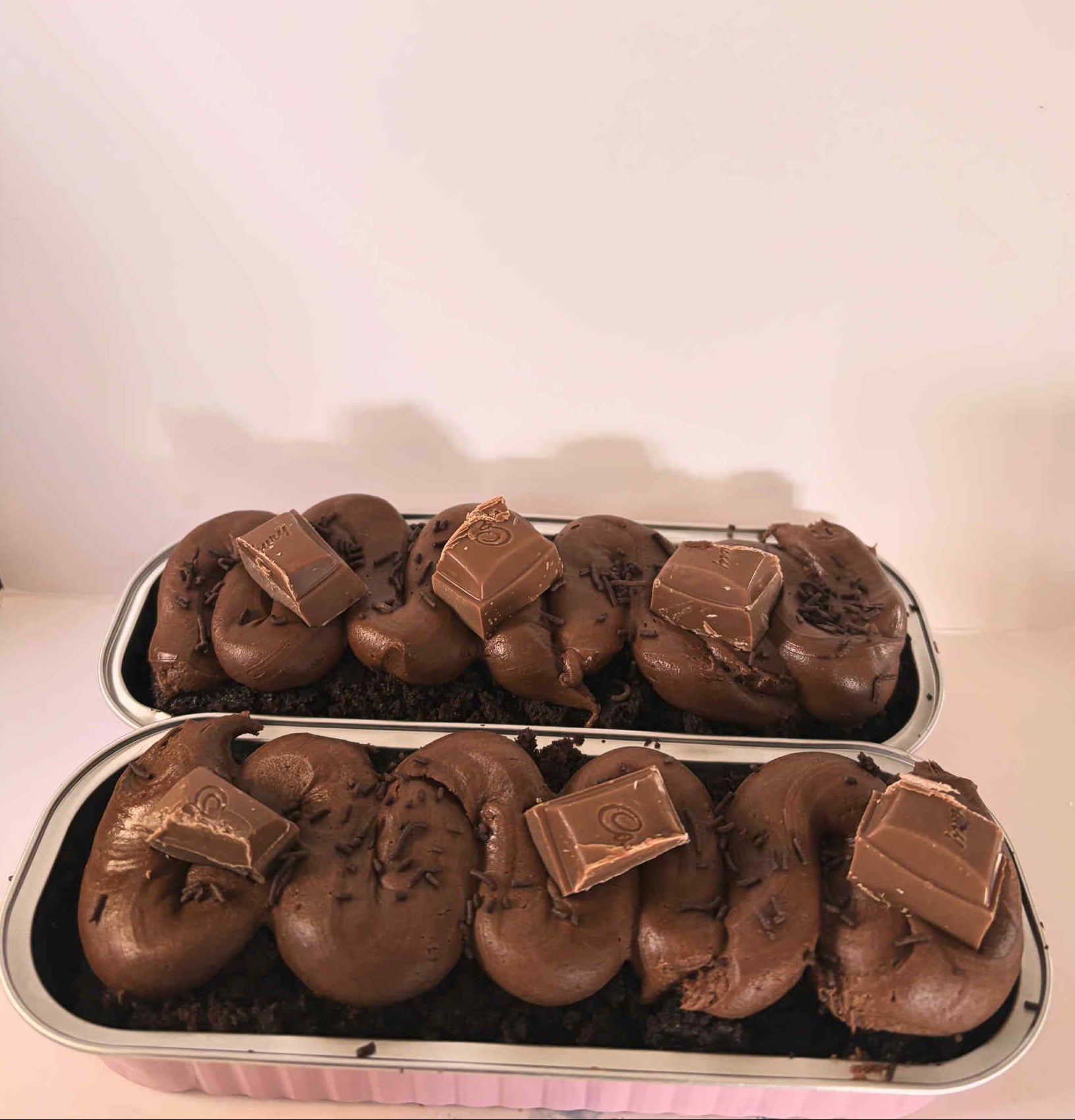 Chocolate cake with chocolate pieces on a metal tray against a white background